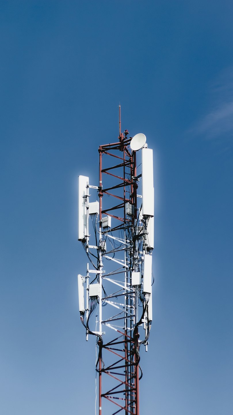 A telecommunications tower with antennas stands against a blue sky.